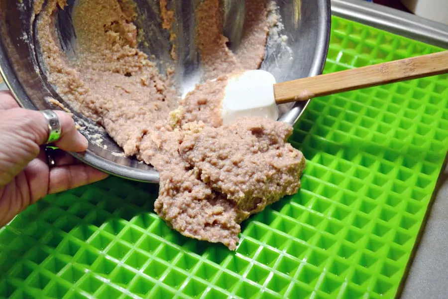 stainless steel bowl with baby food dog treat mixture being put into pyramid mat to bake