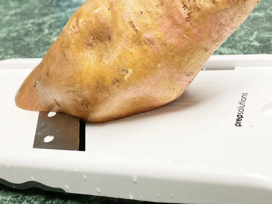Slicing sweet potato on mandolin slicer to make dehydrated dog treats